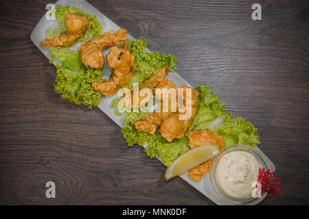 I gamberi fritti su una piastra con salsa e su uno sfondo di legno Foto Stock