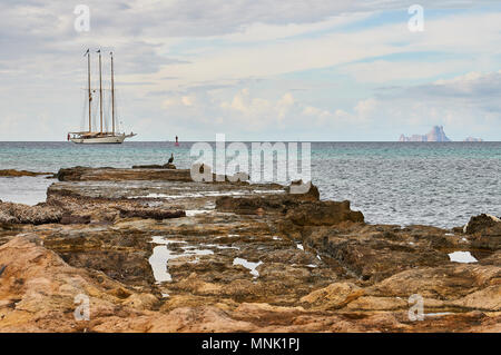 Un classico ancorato in barca a vela con Red Ensign bandiera con un marangone dal ciuffo (phalacrocorax aristotelis) Es Vedrá isolotto (Formentera,Isole Baleari, Spagna) Foto Stock