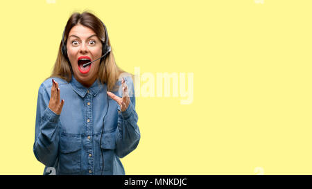 Consulente del centro di chiamata donna nelle cuffie stressante mantenendo le mani sulla testa e atterrito nel panico, urlando Foto Stock