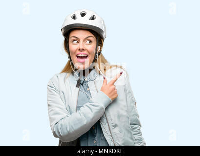 Giovane donna con il casco protettivo e auricolari rivolto lontano lato con un dito Foto Stock