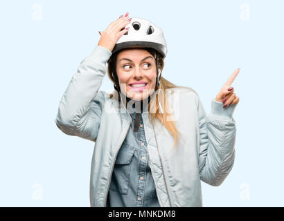 Giovane donna con il casco protettivo e auricolari rivolto lontano lato con un dito Foto Stock
