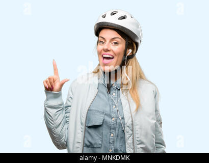 Giovane donna con il casco protettivo e auricolari rivolto lontano lato con un dito Foto Stock