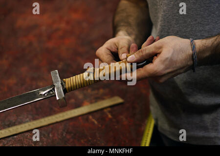 Smith rende avvolgimento in pelle di spada. L uomo è il lavoro in officina. Egli corregge pelle banda su elsa di spada. Foto Stock