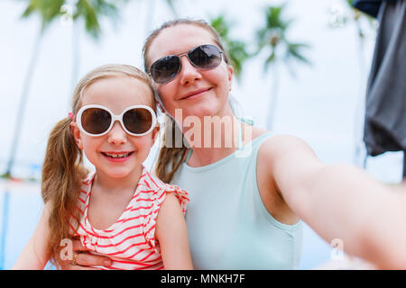 La famiglia felice la madre ed i suoi adorabili poco figlia sulle vacanze estive tenendo selfie con lo smartphone