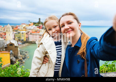 Madre e figlia tenendo selfie con lo smartphone con vista panoramica del villaggio colorato Vernazza, Cinque Terre, Italia sullo sfondo Foto Stock