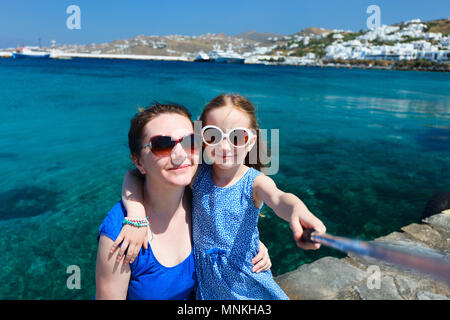 La famiglia felice la madre ed i suoi adorabili poco figlia in vacanza prendendo selfie con un bastone sull'isola di Mykonos, Grecia Foto Stock