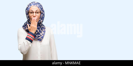 La mezza età araba musulmana donna che indossa il hijab copre bocca in stato di shock, guarda timido, esprimendo il silenzio e confondere i concetti, spaventata isolato sfondo blu Foto Stock