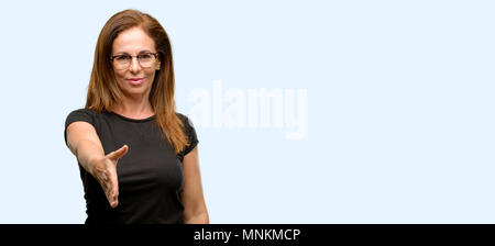 Medioevo donna che indossa la maglia nera e occhiali tiene per mano accogliente nella posa di handshake, esprimendo la fiducia e il concetto di successo, saluto blu isolato Foto Stock