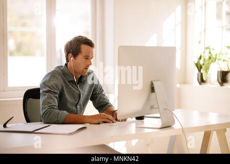Imprenditore lavorando sul computer. Uomo seduto al tavolo di lavoro lavorando sul computer a casa ascolto di audio utilizzando le cuffie. Foto Stock