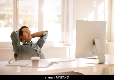 Imprenditore in un momento di relax a casa seduti davanti al suo tavolo di lavoro. L'uomo prendendo una pausa e ascoltare la musica con gli occhi chiusi. Foto Stock