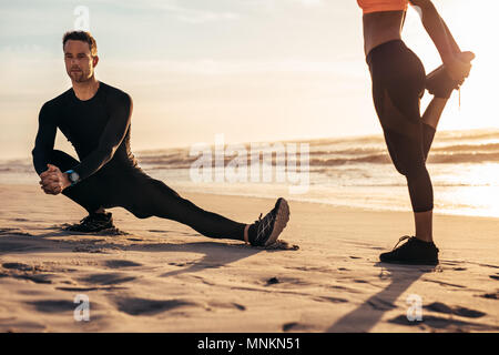 Montare atleta maschio facendo esercizi di stretching sulla spiaggia con la donna. Guide di scorrimento in fase di riscaldamento prima di eseguire in mattina. Foto Stock