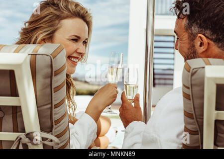 Bella giovane in accappatoi sorridente ad ogni altro e tostatura di bicchieri di vino. Uomo sorridente e donna Accappatoi seduti su sedie a sdraio all'aperto e Foto Stock