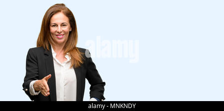 La mezza età della donna in giacca tiene per mano accogliente nella posa di handshake, esprimendo la fiducia e il concetto di successo, saluto isolato sfondo blu Foto Stock