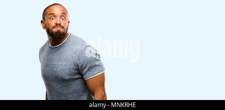 African American uomo con barba sbuffando fuori le guance, avendo divertimento rendendo divertente faccia isolate su sfondo blu Foto Stock