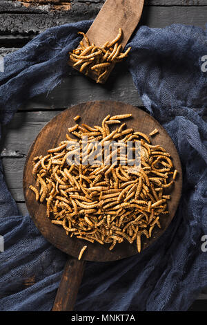 Alta angolazione di una pila di vermi fritte condite con aglio ed erbe aromatiche, in un vassoio di legno su un grigio rustico tavolo in legno Foto Stock