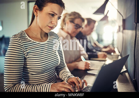 Concentrato di giovani designer che lavorano online con un computer portatile mentre si siede a un tavolo con i colleghi in un ufficio moderno Foto Stock