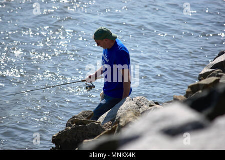 Uomo in blu tee shirt pesca sulla spiaggia rocciosa Foto Stock