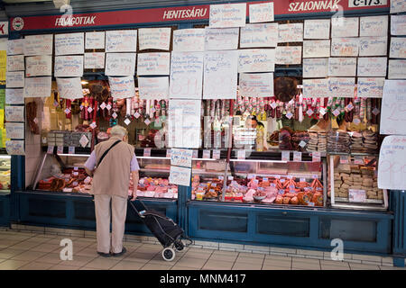 Un uomo non identificato con un carrello in negozi per la carne al mercato centrale nella sezione di Pest di Budapest, Ungheria. Foto Stock