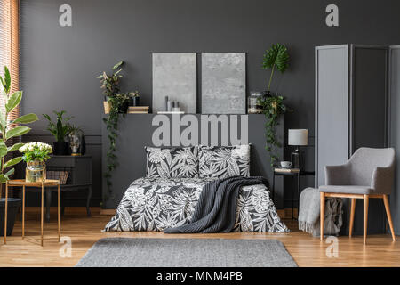 Moderno edificio grigio poltrona con le gambe di legno e una camera del pannello divisorio in un elegante camera da letto interno con arredamento scuro Foto Stock
