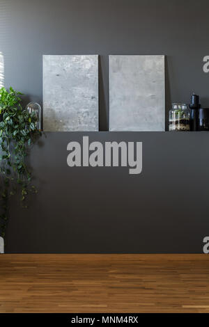 Abstract canvas grigio e un impianto di edera appeso da una vuota parete scura in modo minimalista living room interior Foto Stock