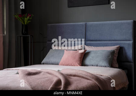 Close-up di rosa e grigio cuscino sul letto con coperte e testiera in interiore camera da letto Foto Stock