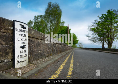 Pietra miliare accanto alla strada deserta sulle rive di Loch Lomond Foto Stock