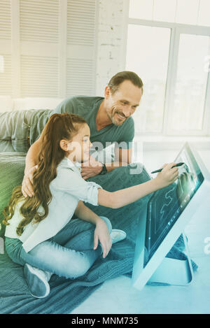 Allegro ragazza il disegno con uno stilo e il suo tipo padre sorridente Foto Stock