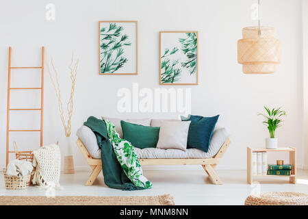 Impianto sul tavolo di legno in folle soggiorno con cuscini di colore verde sul divano beige e dipinti sulla parete Foto Stock