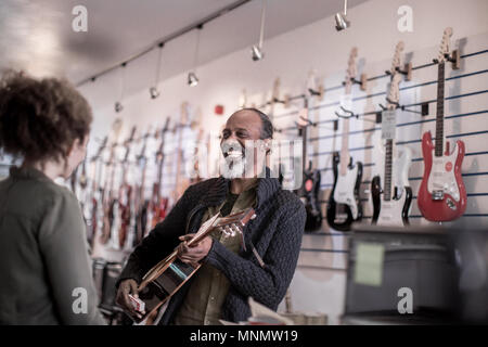 Maschio senior a suonare la chitarra in negozio Foto Stock