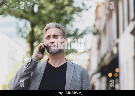 Maschio maturo e a piedi sullo smartphone in città Foto Stock