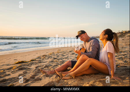 Giovane seduto sulla spiaggia Foto Stock