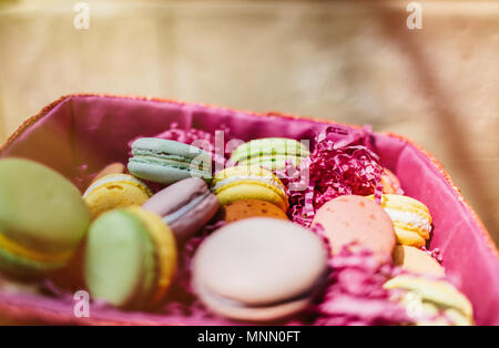 Amaretti colorati e fiori su un tavolo di legno. Dolce macarons in confezione regalo. Lay piatto Foto Stock