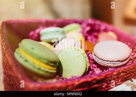 Amaretti colorati e fiori su un tavolo di legno. Dolce macarons in confezione regalo. Lay piatto Foto Stock