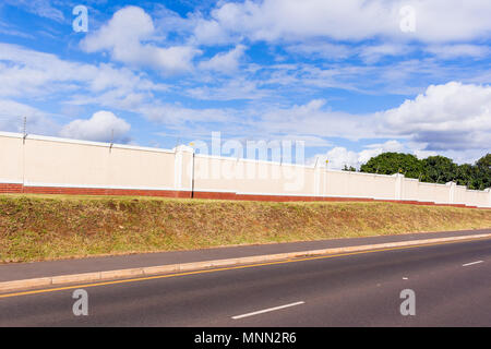 Elettrificate recinto di filo sul lungo muro di cinta della sicurezza per gated propertyalongside residenziale road. Foto Stock
