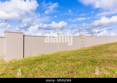 Elettrificate recinto di filo sul lungo muro di cinta della sicurezza per cancelli di proprietà residenziale. Foto Stock