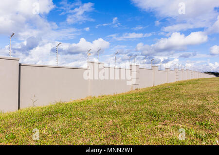 Elettrificate recinto di filo sul lungo muro di cinta della sicurezza per cancelli di proprietà residenziale. Foto Stock