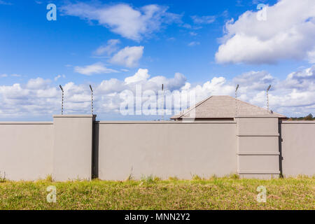 Elettrificate recinto di filo sul lungo muro di confine con la casa dietro gated di proprietà residenziale. Foto Stock