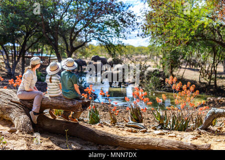 La famiglia di madre e bambini su safari Africano vacanze godendo di osservare la natura a Watering Hole Foto Stock