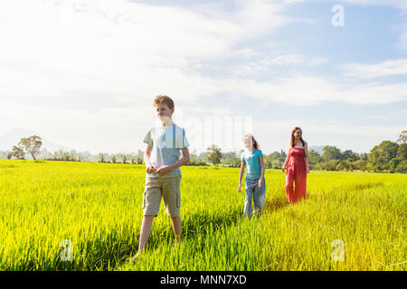 La famiglia di madre e due bambini godendo tranquilla passeggiata in campi di riso con viste mozzafiato sulle montagne in Sri Lanka Foto Stock