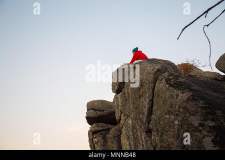 Giovane uomo che fa parkour in piedi sulla roccia e guardando il paesaggio nelle luci del tramonto. Foto Stock