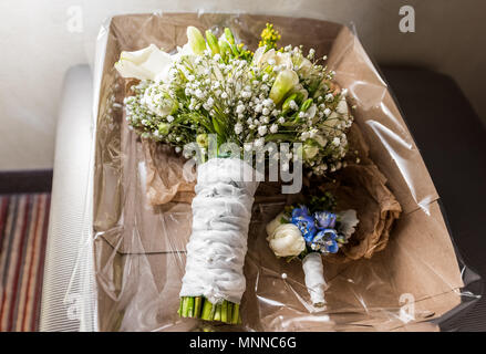 Bouquet nuziali e boutonniere in una scatola di cartone in sera stanza buia, molti fiori, verde giallo e blu di lily giacente su una sedia Foto Stock