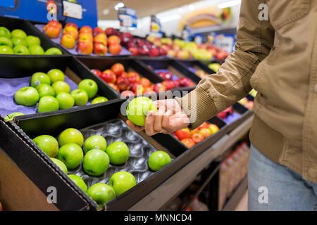 Molte varietà di mele assortiti sul ripiano espositivo in drogheria scatole in corridoio, supermercato interno, uomo persona cliente azienda Granny Smith verde fr Foto Stock