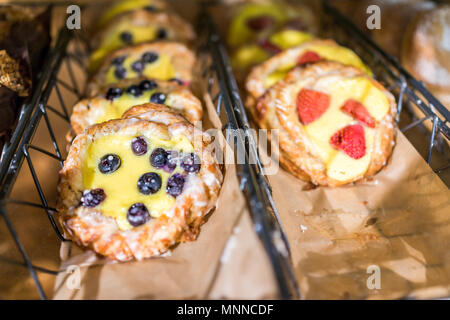 Primo piano di molti giallo crema di formaggio frutti di bosco mirtillo e fragola cotta pasticceria danese sul ripiano display vassoio di dolci in un panificio cafe stor Foto Stock