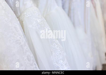 Molti abiti da sposa nella boutique negozio di sconto, bianco gli indumenti appesi su grucce rack fila closeup con pizzo bianco, tulle, design Foto Stock