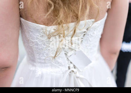 Primo piano posteriore della giovane donna cercando sul Corsetto cucita abito da sposa in boutique di sconto negozio con nastro di legatura, capelli biondi, prezzo di etichetta Foto Stock