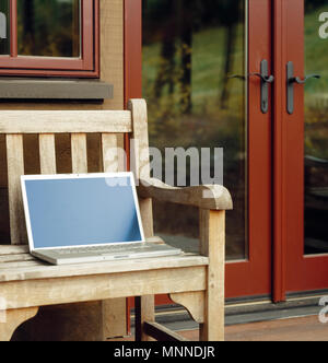 Computer portatile con schermo vuoto sul banco di legno sul ponte o patio di esclusivi home o il resort. Ufficio mobile a lavorare utilizzando la tecnologia wireless all'esterno. Foto Stock