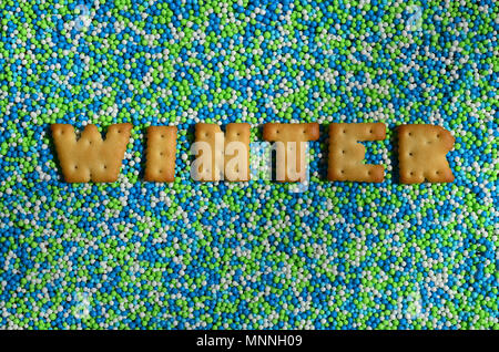 L'inverno. La parola da prodotti commestibili cracker lettere giace sulla polvere di vetrate. Un numero enorme di dolce, perline colorate di dimensioni molto ridotte per la decorazione Foto Stock