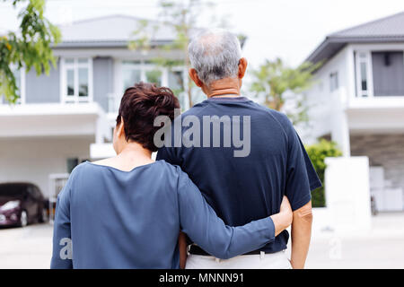 Felice coppia senior da dietro guardando la parte anteriore della casa e auto Foto Stock