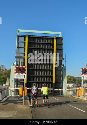 I ciclisti di attendere mentre un ponte stradale sulla Baia di Cardiff barrage è in posizione sollevata. I ponti di sollevamento per permettere il passaggio alle barche in nelle serrature Foto Stock