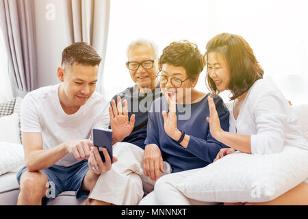 Famiglia asiatica con figli adulti e genitori anziani facendo una chiamata video e agitando al chiamante a casa Foto Stock